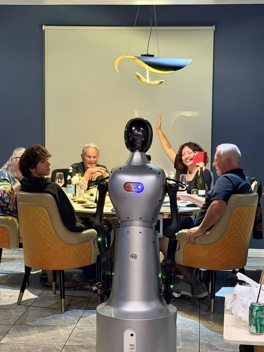 Guests waving at StarBot Nova during a group dinner